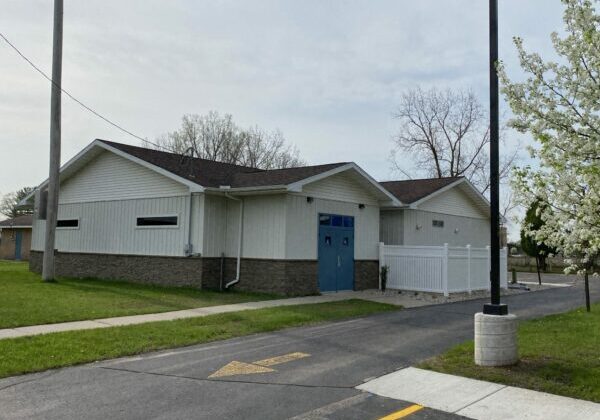 Small white building with blue doors and fence.